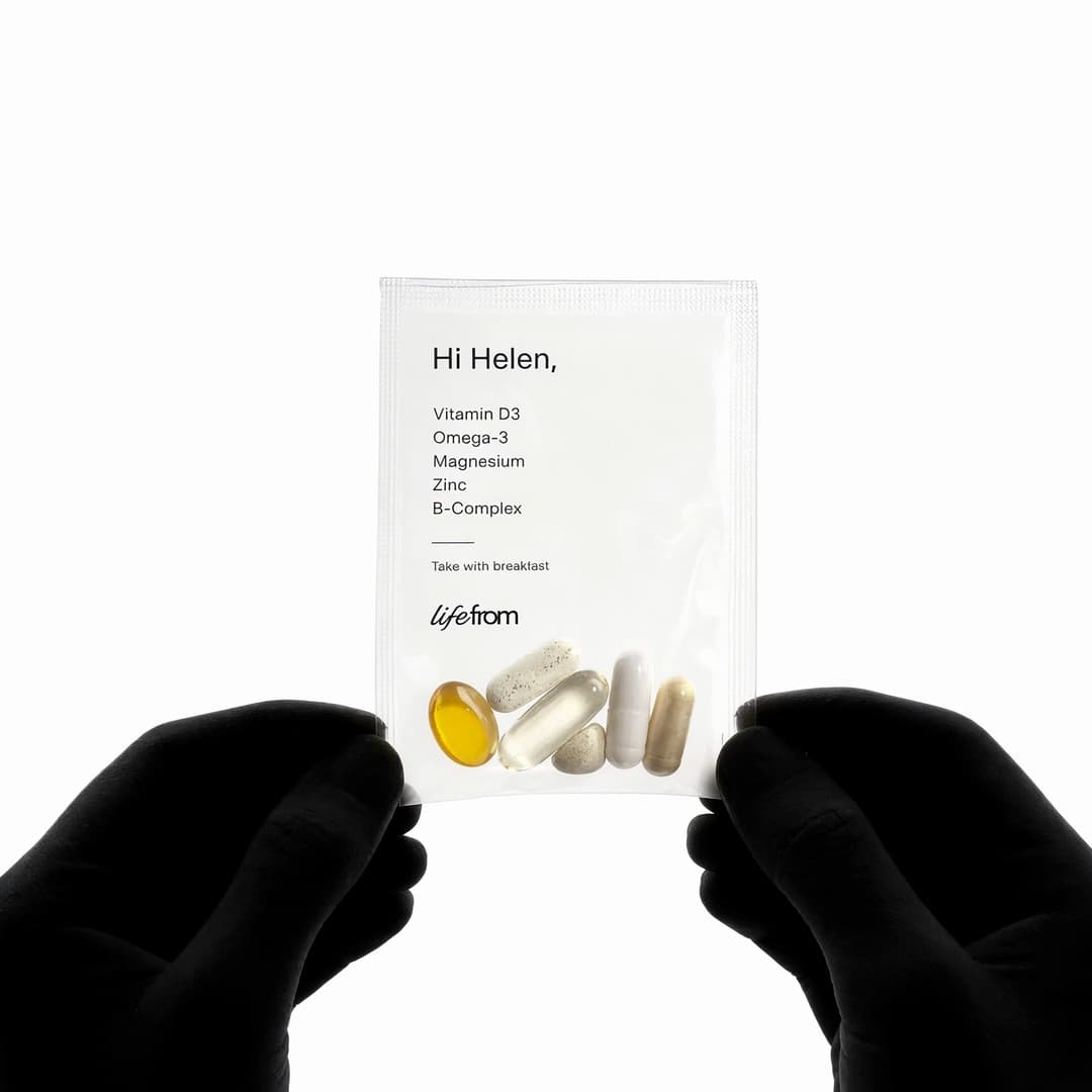 Gloved hands holding a personalised LifeFrom pouch with five supplements
